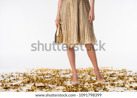 cropped image of girl standing on confetti in skirt and holding bottle of champagne