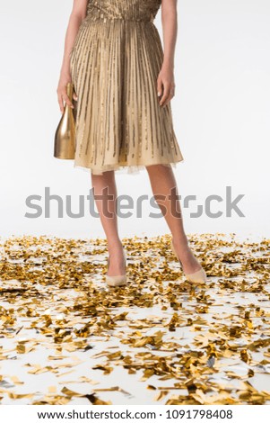 cropped image of woman standing on confetti in dress and holding golden bottle of champagne