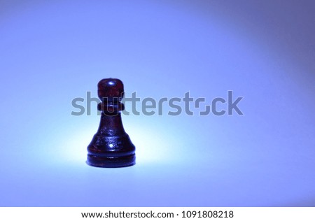 
Close-up of a wooden chess piece of a black pawn on a neutral blue background. A usual soldier of the army of the king.
