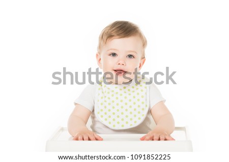 smiling baby boy in bib sitting in highchair isolated on white background  Royalty-Free Stock Photo #1091852225