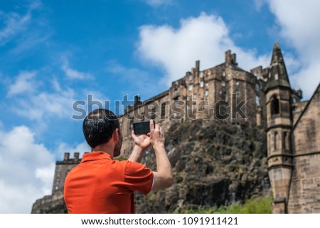 Tourist taking mobile phone pictures of Edinburgh Castle in spring time.