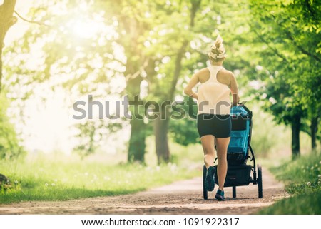 Running woman with baby stroller enjoying summer day in park. Jogging or power walking supermom, active family with baby jogger. Royalty-Free Stock Photo #1091922317