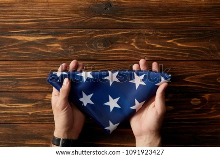 cropped shot of man holding folded american flag on wooden background