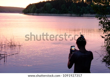 girl takes pictures of the river at sunset on the phone