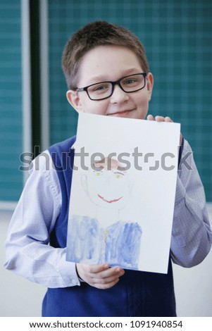 Drawing lesson in an elementary school. A child shows a sheet of paper with a picture looking at the camera and smiling. The concept of primary education.