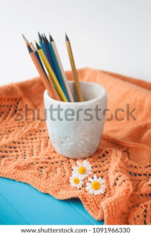 Wooden bright pencils, orange plaid, three flowers of chamomile and a glass of handmade on a blue wooden background.