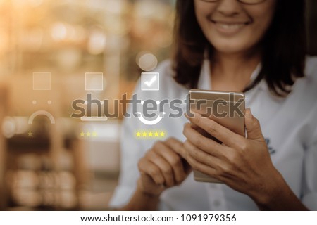 Businesswoman pressing face emoticon on virtual touch screen at smartphone .Customer service evaluation concept. Royalty-Free Stock Photo #1091979356