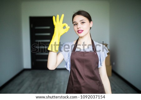 Young woman as cleaning maid holding liquids and showing OK sign at home