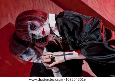 Actress with zombie makeup near mirror on red background