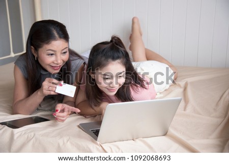 Mother and daughter are shopping on line through lab top in bedroom.