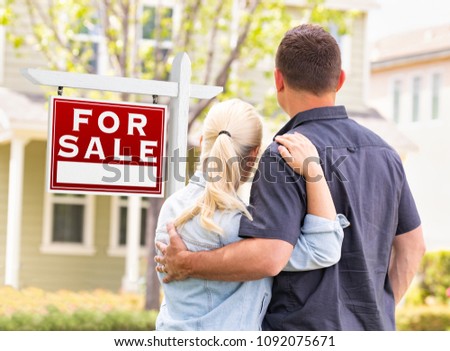 Caucasian Couple Facing Front of Sold Real Estate Sign and House.