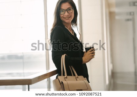 Portrait of asian business woman standing by a railing with coffee and purse. Attractive woman standing in office.