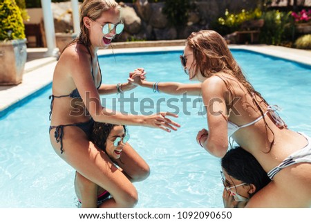 Women in bikinis having fun in swimming pool. Girls sitting on their friends shoulders and fighting in a pool.