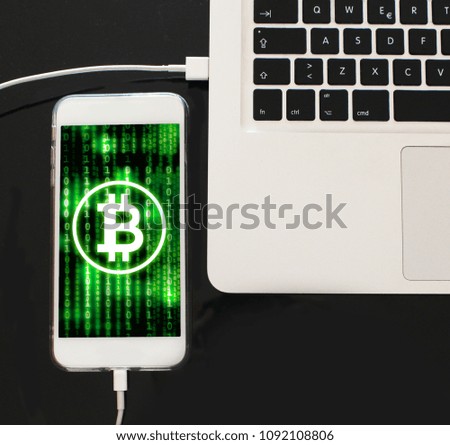 Bitcoin and binary code in smartphone screen plugged to a computer