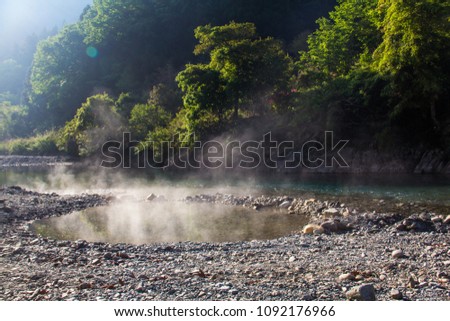 An outdoors river side natural hot spring pool onsen with steam rising from it in morning sun, in Kawayu,  Hongu, Wakayama, on the Kii Peninsula, at the end of the Kumano Kodo hiking trail, Japan. Royalty-Free Stock Photo #1092176966