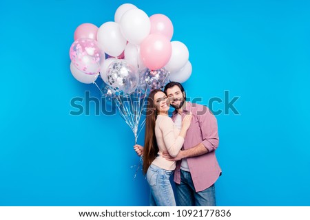 Portrait of positive attractive partners holding pink and white air balloons, man with bristle woman with long hair isolated on bright blue background