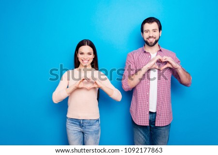 Portrait of cheerful joyful partners in casual outfits jeans showing heart figure love signs with fingers looking at camera isolated on vivid blue background