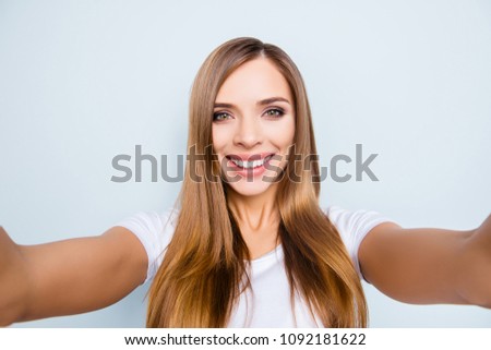 Self portrait of cute positive girl with long hair shooting selfie on front camera with two hands  isolated on grey background