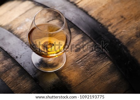 Snifter glass of brandy standing on an oak barrel in a cellar Royalty-Free Stock Photo #1092193775