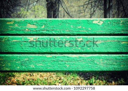 Wooden boards with peeling green paint. Behind them is a forest with trees and grass. An unusual photo with a place for text in the center.
