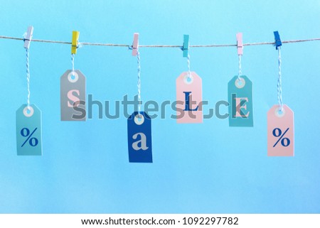 Labels hang on the rope with attached clothespins. They inscription SALE. Bright photo on a blue background.