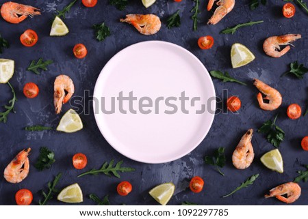 On a dark textured background there is an empty pink plate, food is scattered around. Shrimp, lemon and greens. Mock up, space for text. Tinted photo in low key.