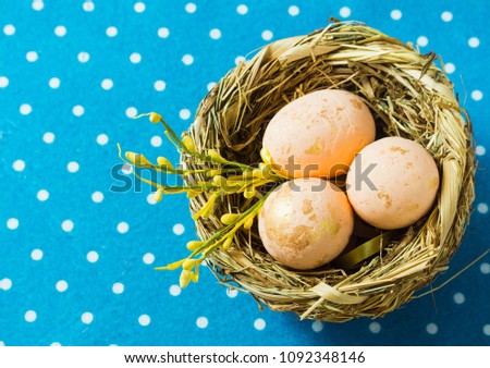 nest with three pink eggs with small yellow flowers on blue with white polka dots napkin. happy easter top view with copy space