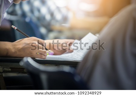 soft focus.hand high school or university student in uniform holding pencil writing on paper answer sheet.sitting on lecture chair taking final exam or study attending in examination room or classroom Royalty-Free Stock Photo #1092348929