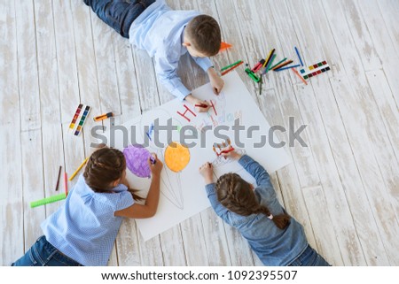 Top view creative photo of little boy and girl on brown wooden floor. children draw together on a large sheet of paper