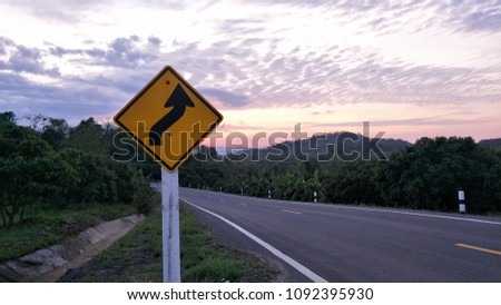 Yellow guide post sits beside road among blue sky and mountain in the evening.background.