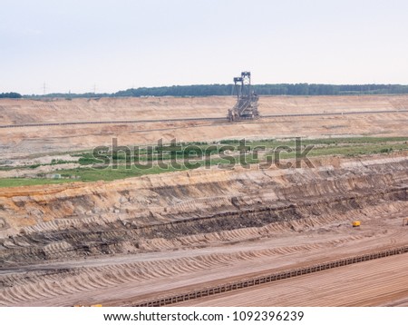 Brown coal open pit, earth layers with excavator in the picture. Hambach Forest in the background.