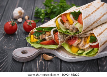 Tortilla wraps with grilled chicken and fresh vegetables on a wooden board. Mexican fast food background.