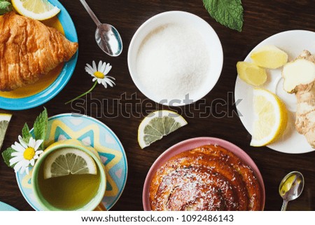 Herbalal tea with lemon and mint leaves, ginger root and croissant on the wooden background