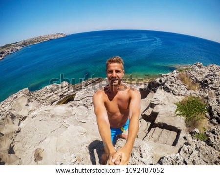 Partly blurred image because of drops of water. Young male explorer in adventure ready for snorkeling. Selfie shot at summer day at rock in the middle of the sea.