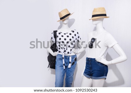 Two mannequin in female shirt with blue ,shorts jeans,sunglasses, handbag,hat, –wooden background
