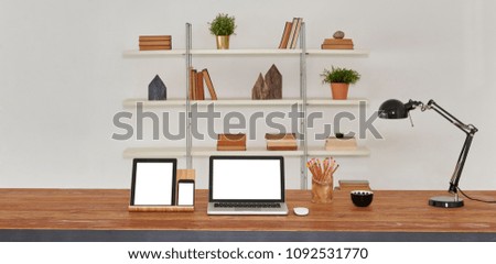 laptop and tablet on the wood table and office interior. Bookcase background with home accessory book vase of flowers.