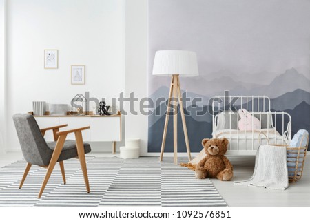 A wooden floor lamp and a modern gray armchair in a monochromatic child's bedroom interior in scandinavian style