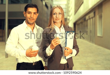 Businesswoman and her partner are standing with folder and coffee near the office.