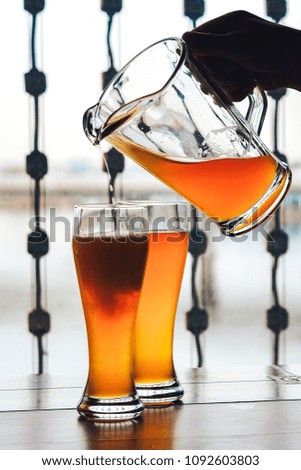 Two glass beer on wood background with copyspace. Two glasses of wheat beer. A man's hand pours beer from a decanter into one of glasses