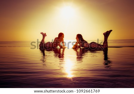 Two beautiful girls enjoy in the infinity pool in sunset. Maldives.