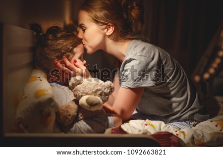  mother puts her daughter to bed and kisses her in the evening
