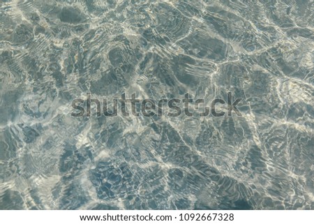 Shimmering sun glares on pebble seabed under clear water of shallow of sea beach as natural background