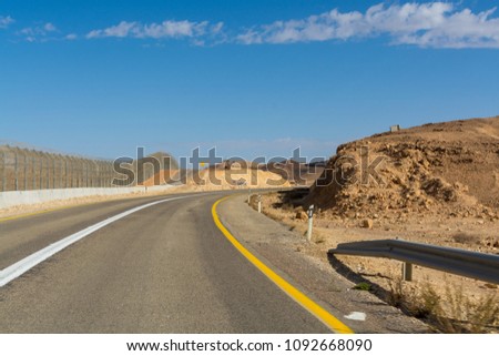 Asphalt road in desert Negev, Israel, road 12, transport infrastructure in desert, view on fence wall on boarder with Egypt, scenic mountains route from Eilat to north of Israel