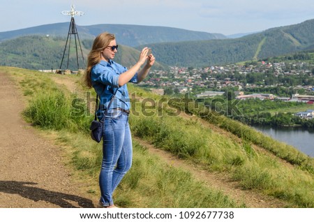 A young girl in blue clothes, wearing sunglasses, takes pictures in the summer on the street