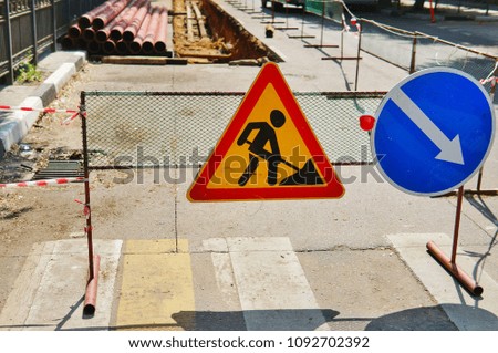 Road signs "Repair work" and "Detour on the right" on the background of a trench dug in the road for laying water pipes
