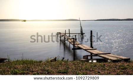 Beautiful picture on a small jetty bridge / pier in a lake. Sunset and backlit in the evning. Long / slow shutter speed making the water surface smooth.