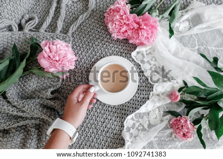 girl holding a cup of coffee with peonies on a gray plaid. Flat-lay of cup of coffee with  peonies