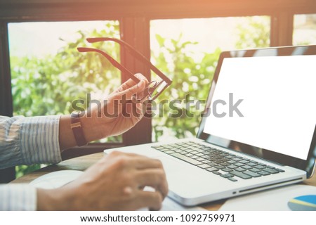 Business man hands hold glasses and using laptop with blank screen on desk in cafe. instagram style filter photo vintage tone