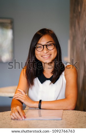 Professional business portrait of an attractive, young Chinese Asian woman. She and is wearing nerdy spectacles and is smiling for her head shot.