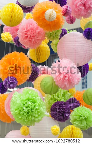 Bright decorations of paper colored POM-poms. POM-poms made of paper hanging from the ceiling. Background of colored spots.